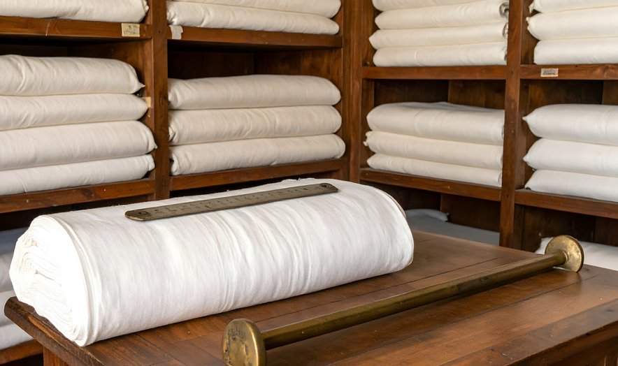 Shelves of folded white linens behind a rolled textile
